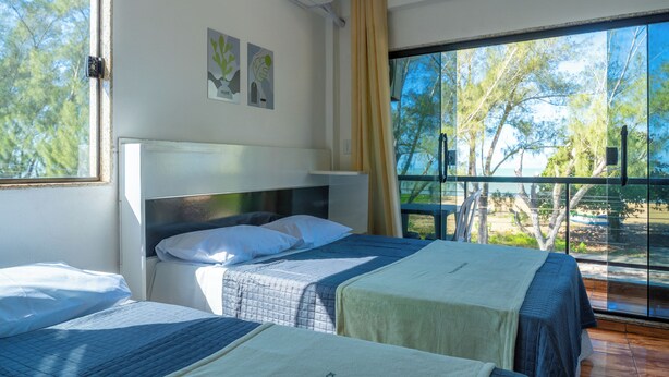 Ein Hotelzimmer mit zwei Betten, einem großen Fenster mit Blick auf Bäume und einem Balkon.