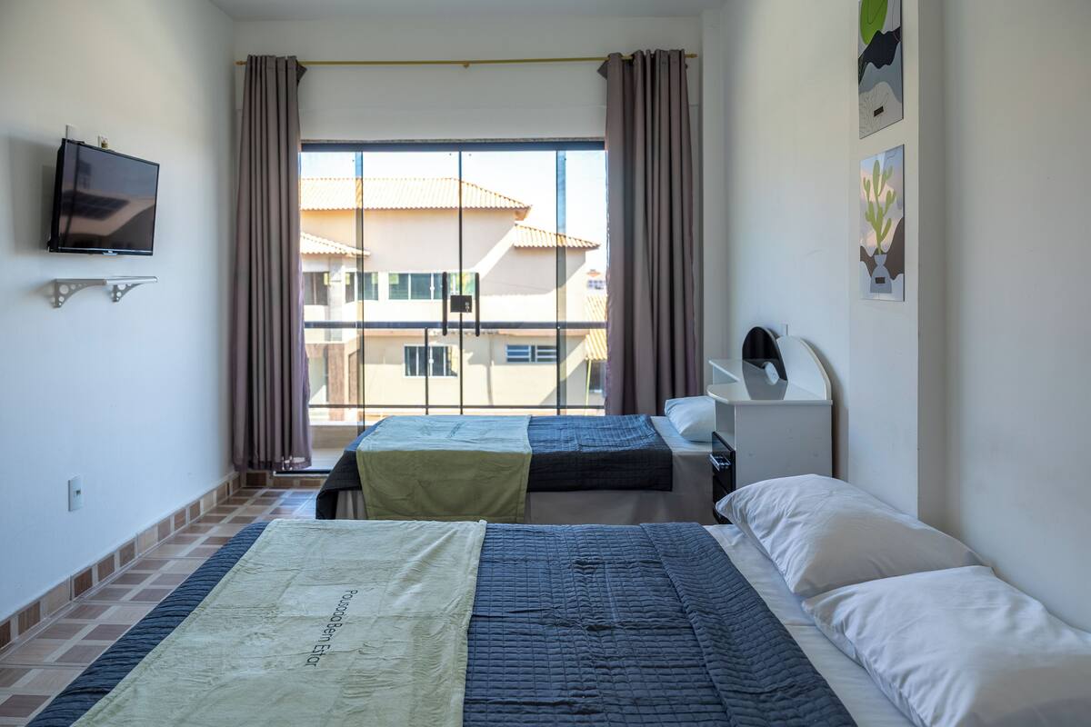 Een hotelkamer met twee bedden, een televisie en een raam met gordijnen.