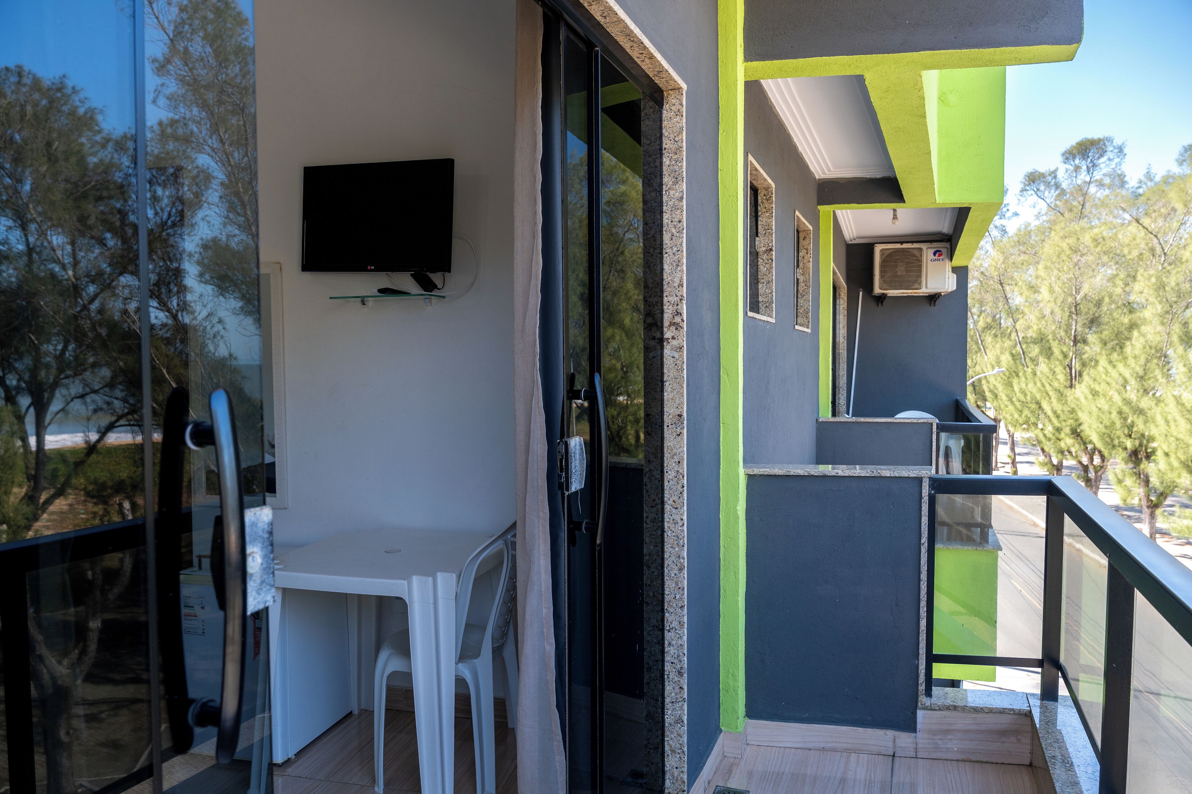 Un balcon avec une porte vitrée, une table blanche et un téléviseur fixé au mur.