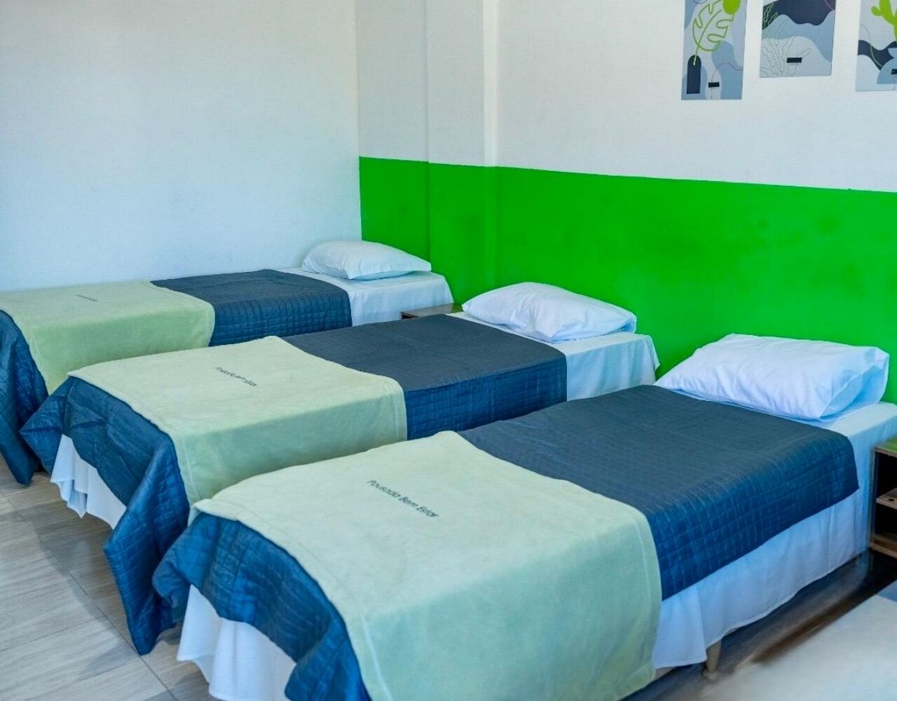 A room with four single beds arranged in a row, each with a green and blue bedspread.