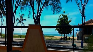 Blick aus einem Gebäude durch ein Fenster auf einen Strand, Palmen und einen strahlend blauen Himmel.