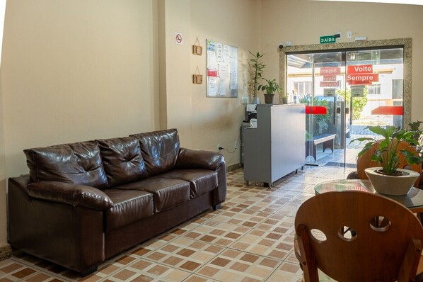 A reception area with a brown leather sofa, a wooden chair, a reception desk, and a bulletin board. - Pousada Bem Estar offshore (Campos)