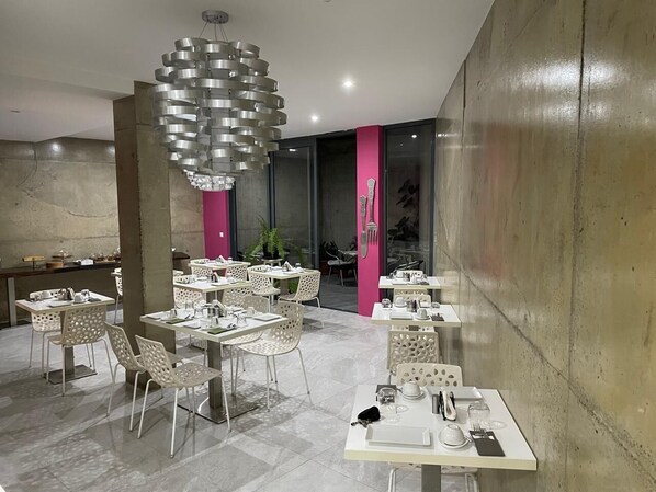 Un comedor moderno con mesas y sillas blancas, una lámpara circular original y una pared de concreto.