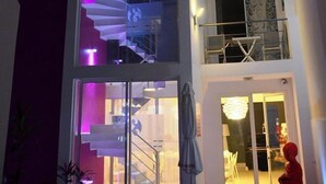 Un immeuble à plusieurs étages doté d’un escalier en colimaçon central, illuminé par des lumières violettes.