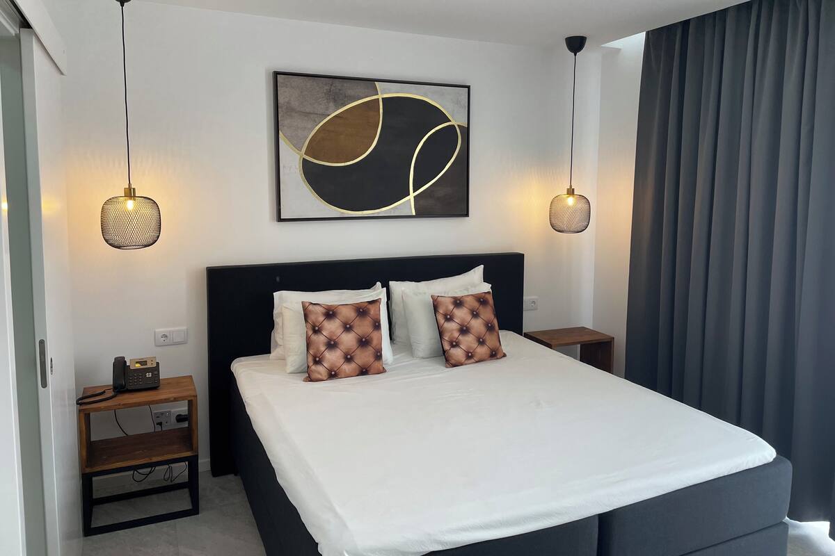 A modern bedroom with a large bed, two bedside tables, a wall-mounted artwork, and a ceiling light fixture.