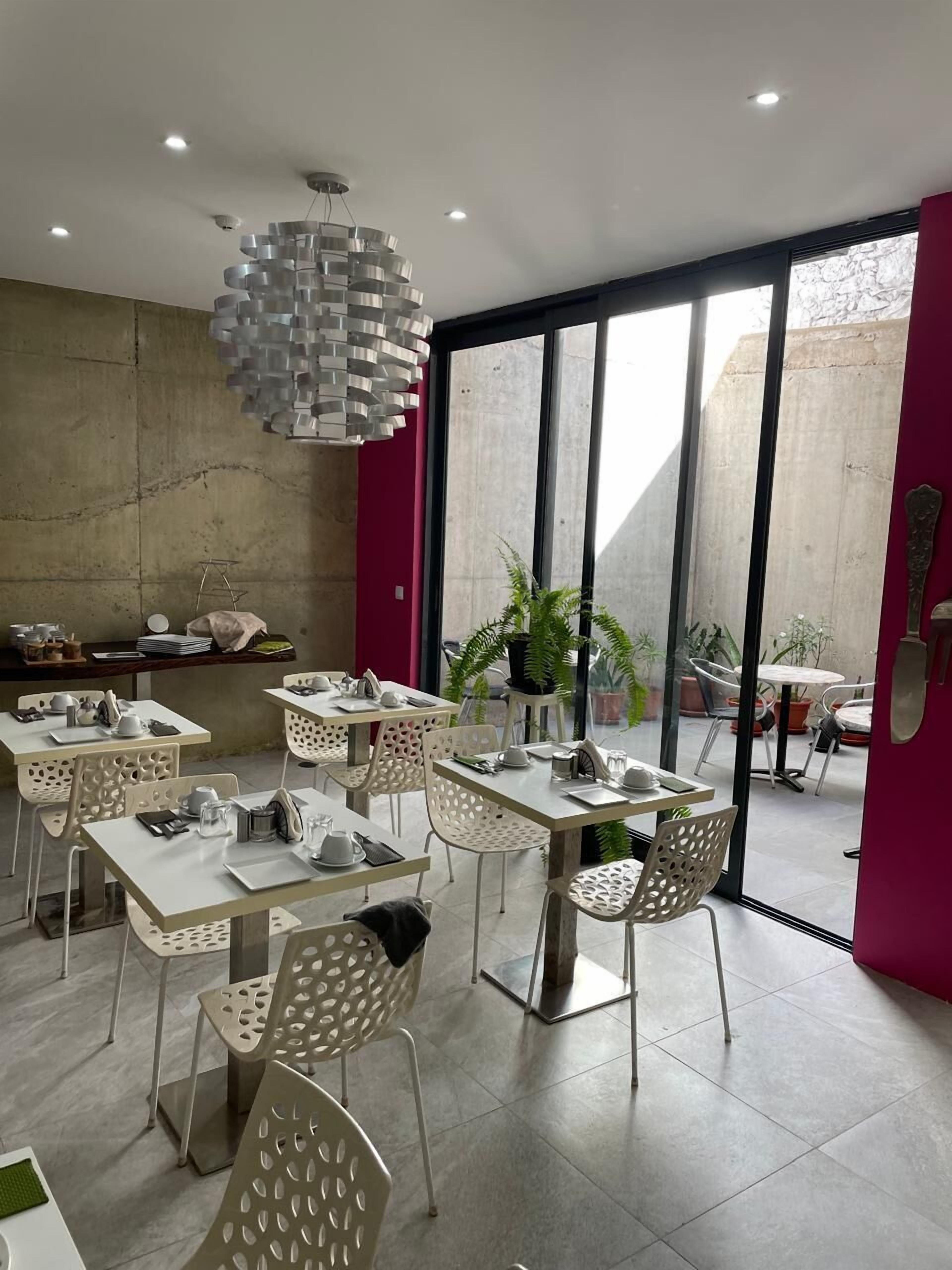 Un comedor moderno con mesas y sillas blancas, una lámpara de techo original y amplias ventanas que ofrecen vistas al exterior.