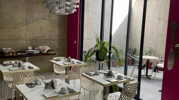 Un comedor moderno con mesas y sillas blancas, una lámpara de techo original y amplias ventanas que ofrecen vistas al exterior.