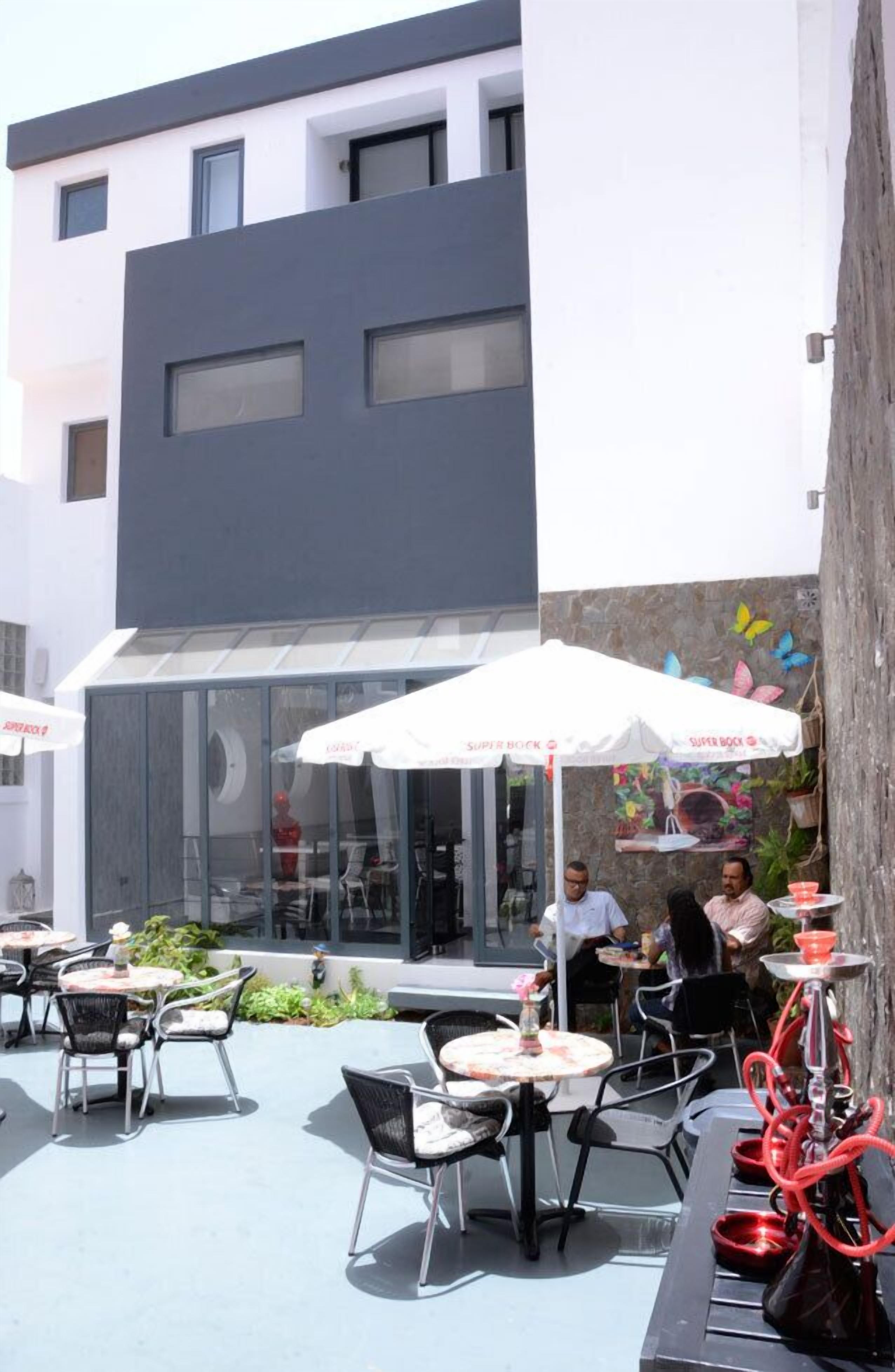En udendørs café med borde, stole og et glaslysehus, samt et muralmaleri på væggen.
