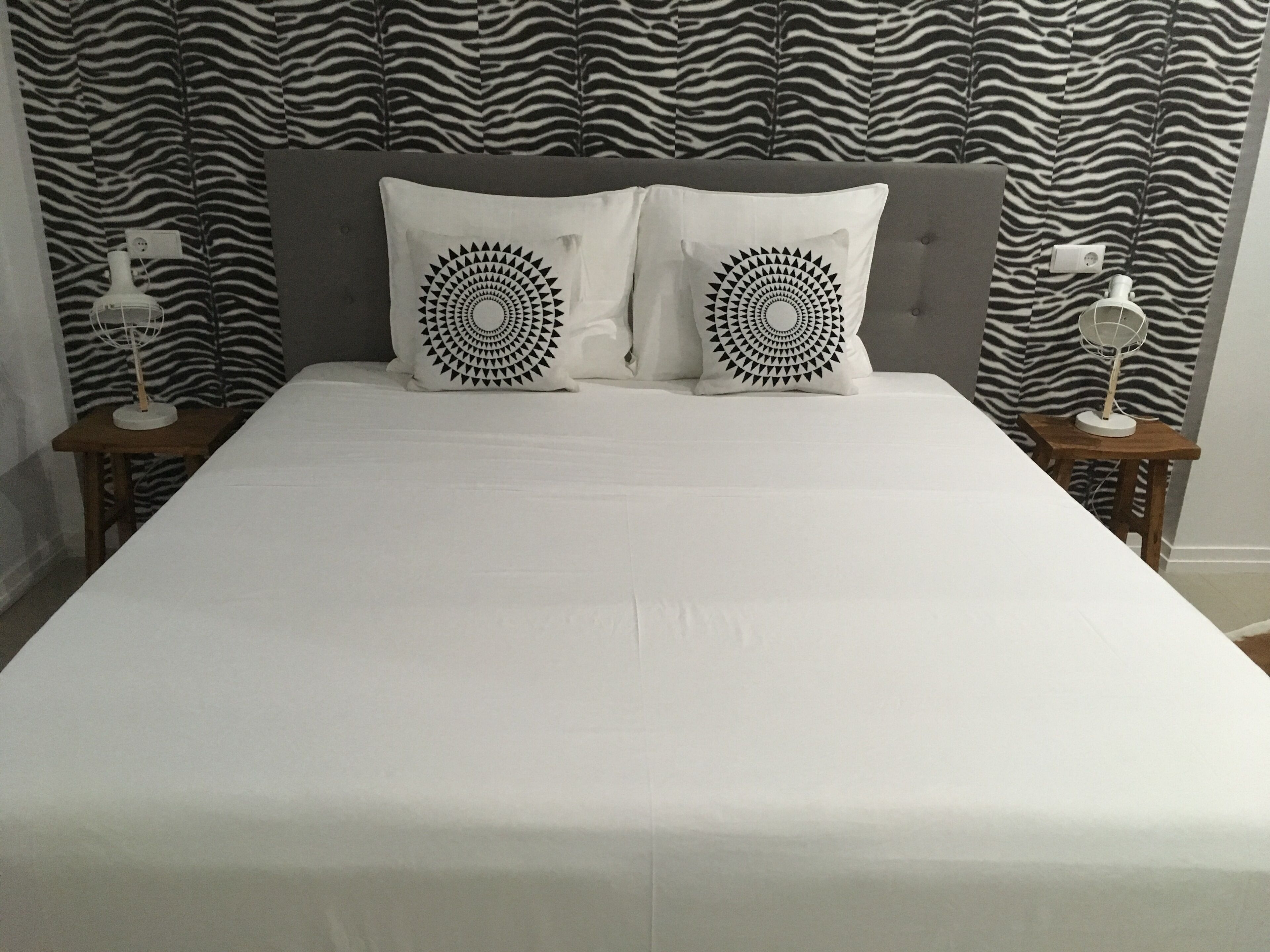 Een bed met een hoofdbord met zebraprint, twee decoratieve kussens en nachtkastjes met lampen.