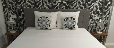 Un lit avec une tête de lit à motifs zébrés, deux coussins décoratifs et des tables de chevet avec des lampes.