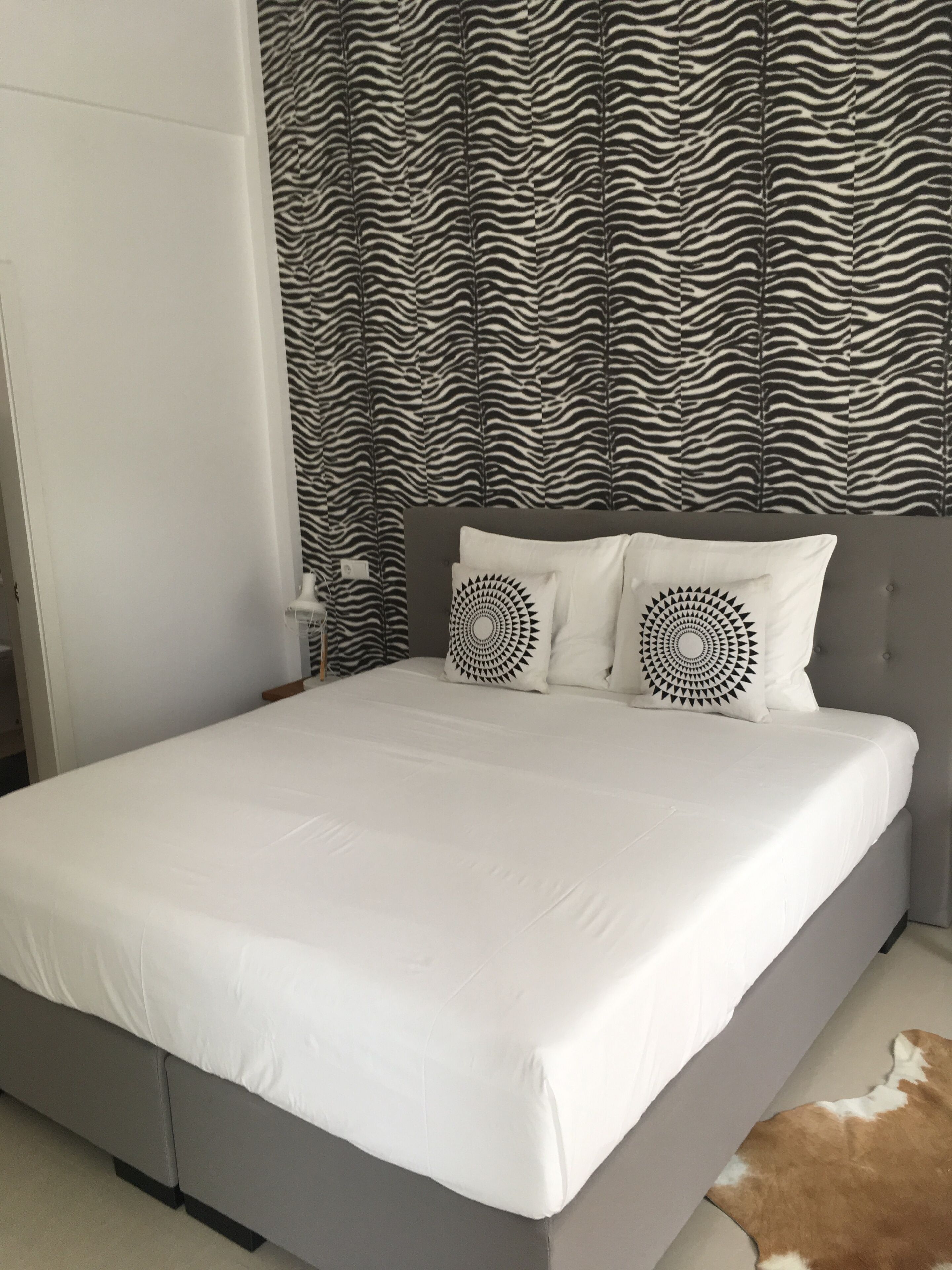 Een bed met wit beddengoed, twee ronde kussens en een gordijn met zebraprint.