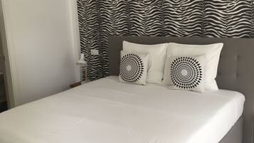 Een bed met wit beddengoed, twee ronde kussens en een gordijn met zebraprint.