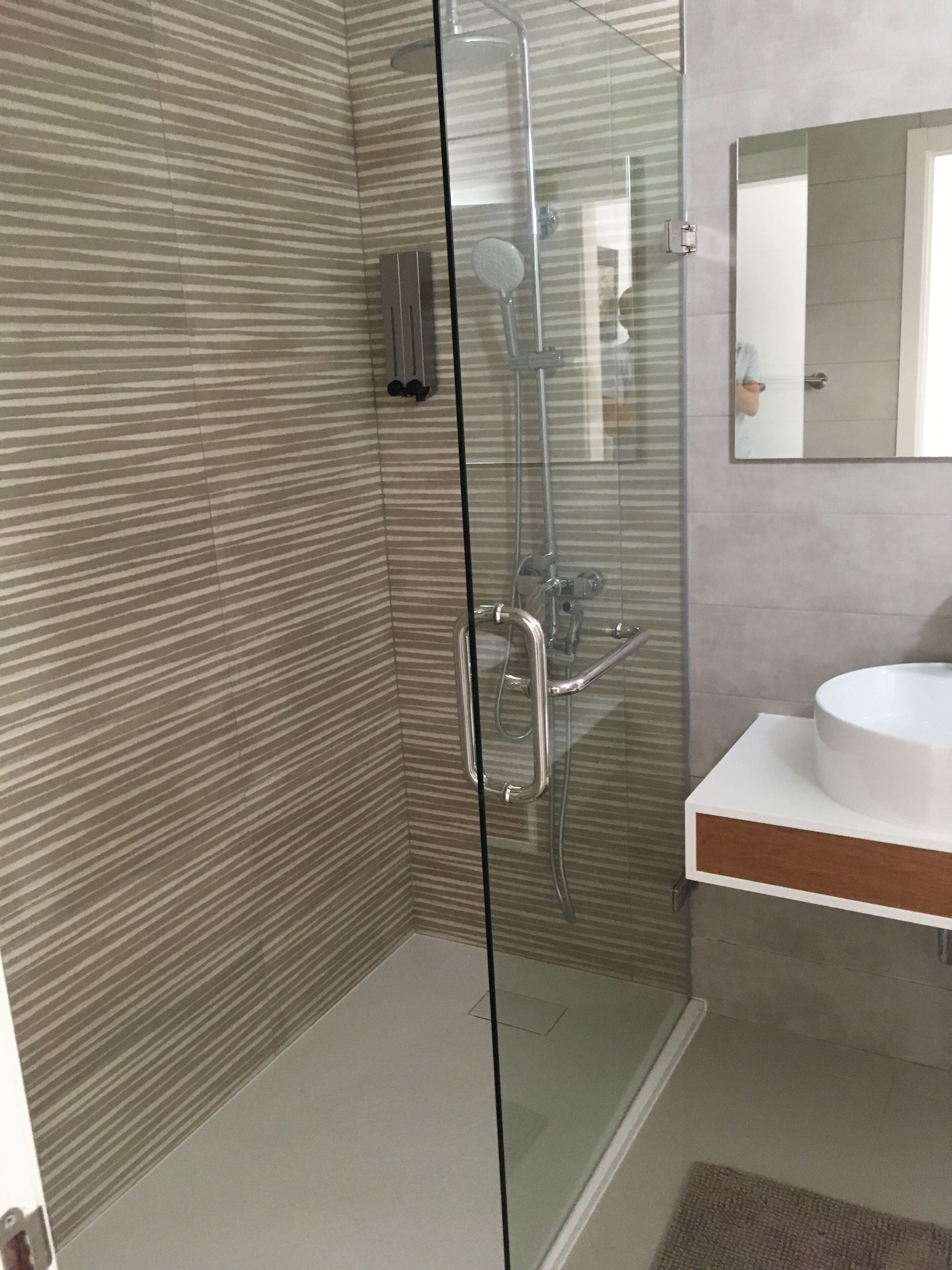 Un baño moderno con ducha envuelta en vidrio, un lavabo blanco y azulejos a rayas en la pared.