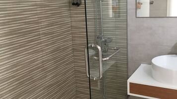Un baño moderno con ducha envuelta en vidrio, un lavabo blanco y azulejos a rayas en la pared.