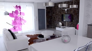 Ett modernt vardagsrum med en vit soffa, ett runt soffbord och ett matbord i glas. Det finns en vägg av sten och en platt-TV som är monterad på väggen.
