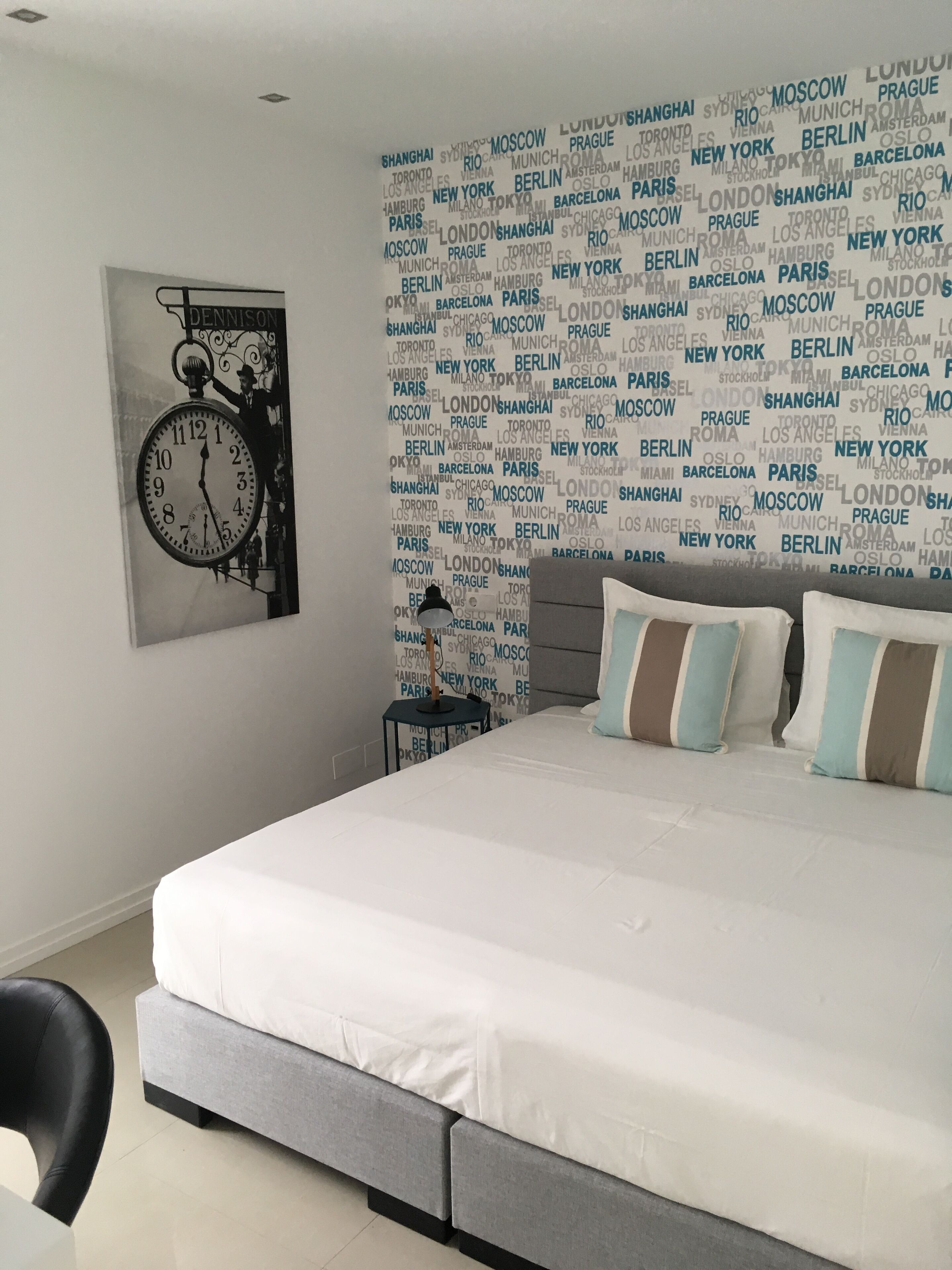 Un dormitorio moderno con una cama grande, un reloj y una pared con nombres de ciudades.