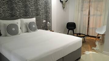 Ein Schlafzimmer mit einem Kopfteil in Zebramuster, einem Bett mit weißer Bettwäsche, einem schwarzen Stuhl, einem weißen Stuhl und einem an der Wand befestigten Stierkopf.