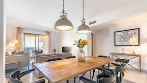 A modern dining area with a wooden table, black chairs, and pendant lights. There is a vase with sunflowers on the table. - Sea Views and Garden in Señorio de Cifuentes (Benahavís)