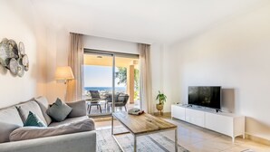 A modern living room with a sofa, coffee table, TV, and a view of the outdoors. - Sea Views and Garden in Señorio de Cifuentes (Benahavís)