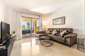 Un soggiorno con divano, tavolino, televisore e vista panoramica attraverso una porta vetrata.