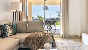 A modern living room with a sofa, a lamp, and a view of the outdoors through a sliding glass door. - Premium 2BR with Beautiful Terrace & Sea Views (Benahavís)