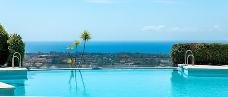 En klar, blå swimmingpool med udsigt til havet og et fjerntliggende landskab.