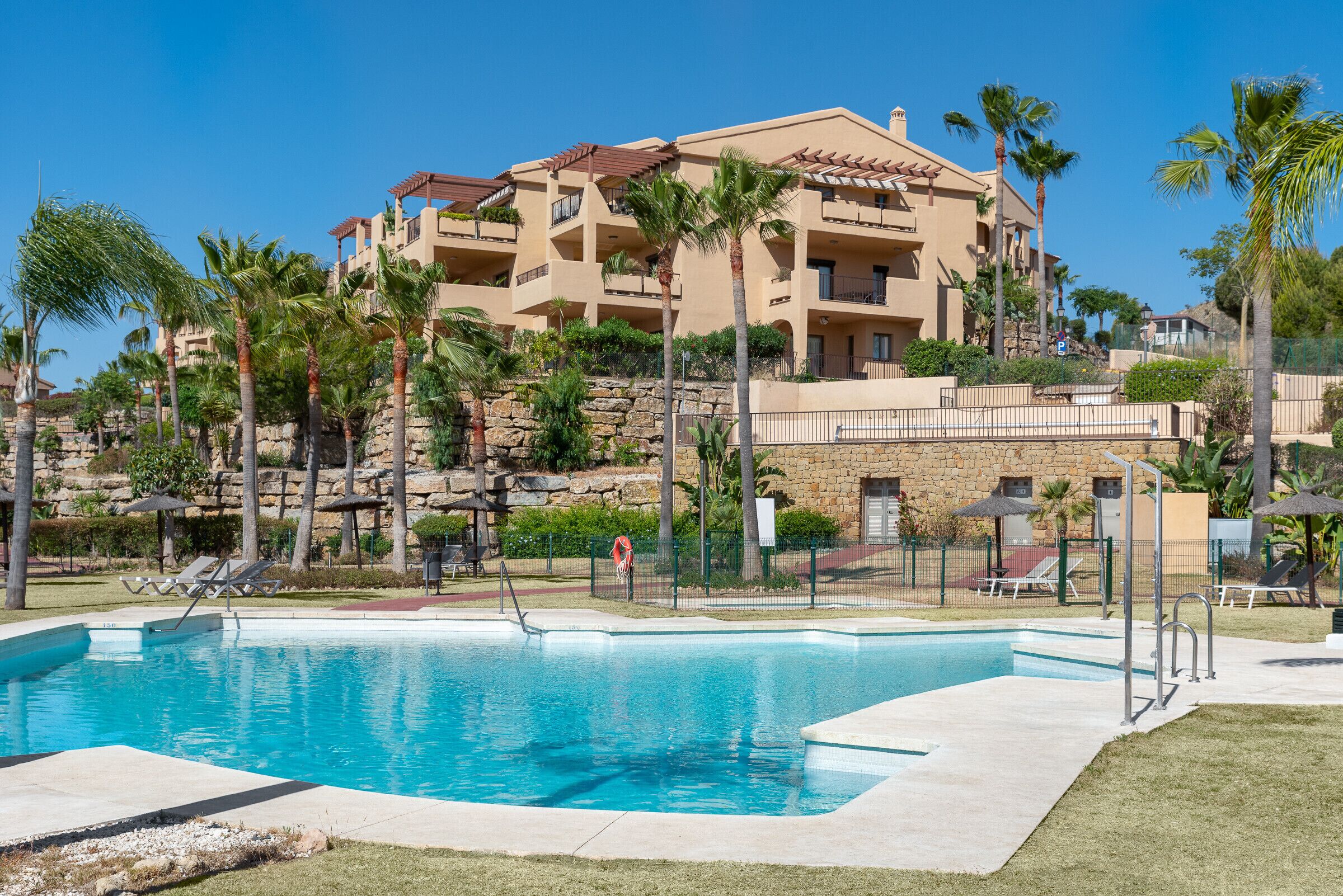 Un hôtel doté d’une piscine, de palmiers et d’un mur en pierre.