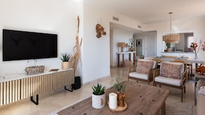 En moderne stue med et stort fladskærms-TV, et trækonsolbord og et spiseområde med træstole og et bord.