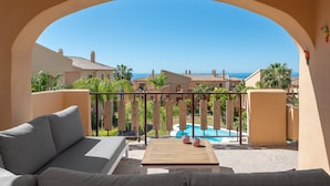 A balcony with a view of a swimming pool and the sea, a wooden table, and a grey sofa. - Charming 2BR with Beautiful Sea Views (Benahavís)