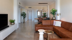 A modern living room with a brown leather sofa, a flat-screen TV, and a dining area in the background. - Charming 2BR with Beautiful Sea Views (Benahavís)