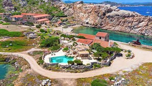 Un complejo turístico frente al mar con piscina, terreno rocoso y vistas al océano.