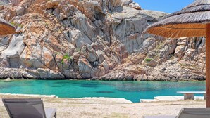 Una playa con agua turquesa cristalina, acantilados rocosos y sillas de descanso.