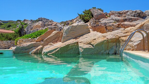 Una piscina cristalina con una pared de piedra y una escalera metálica para entrar.