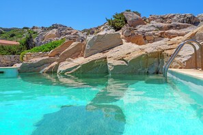 A clear pool with a stone wall and a metal ladder leading into it. - Villa Itaca - Amazing Swimmingpool by the Sea (la maddalena)