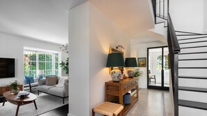 A modern living room with a sofa, coffee table, and a console table with lamps. A staircase is visible to the right.