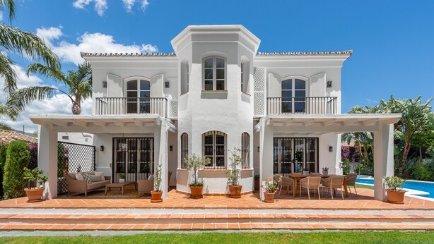 A two-story house with a covered patio, outdoor furniture, and a swimming pool.