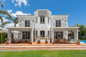Una casa de dos pisos con un porche cubierto, mobiliario exterior y una piscina.