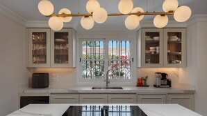 A modern kitchen with a central island, white cabinetry, and a view through a window with a metal gate.