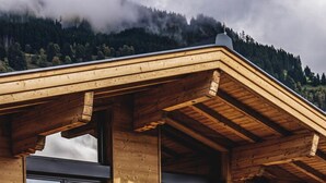 A wooden cabin with large windows and a balcony overlooking a mountainous landscape. - Chalet Amadeus - Designer Luxury Chalet for 14 (Piesendorf)