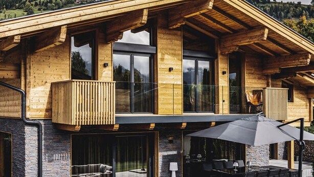 A modern wooden house with a balcony, outdoor seating, and a stone wall. - Chalet Amadeus - Designer Luxury Chalet for 14 (Piesendorf)