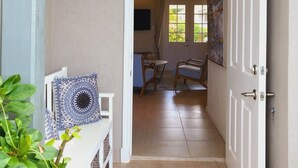 A doorway leading to a room with a dining table and chairs, a bench with a patterned cushion, and a door with a metal handle. - Villa Vuemont - Peaceful 3 Bedroom Villa With Pool (Speightstown)