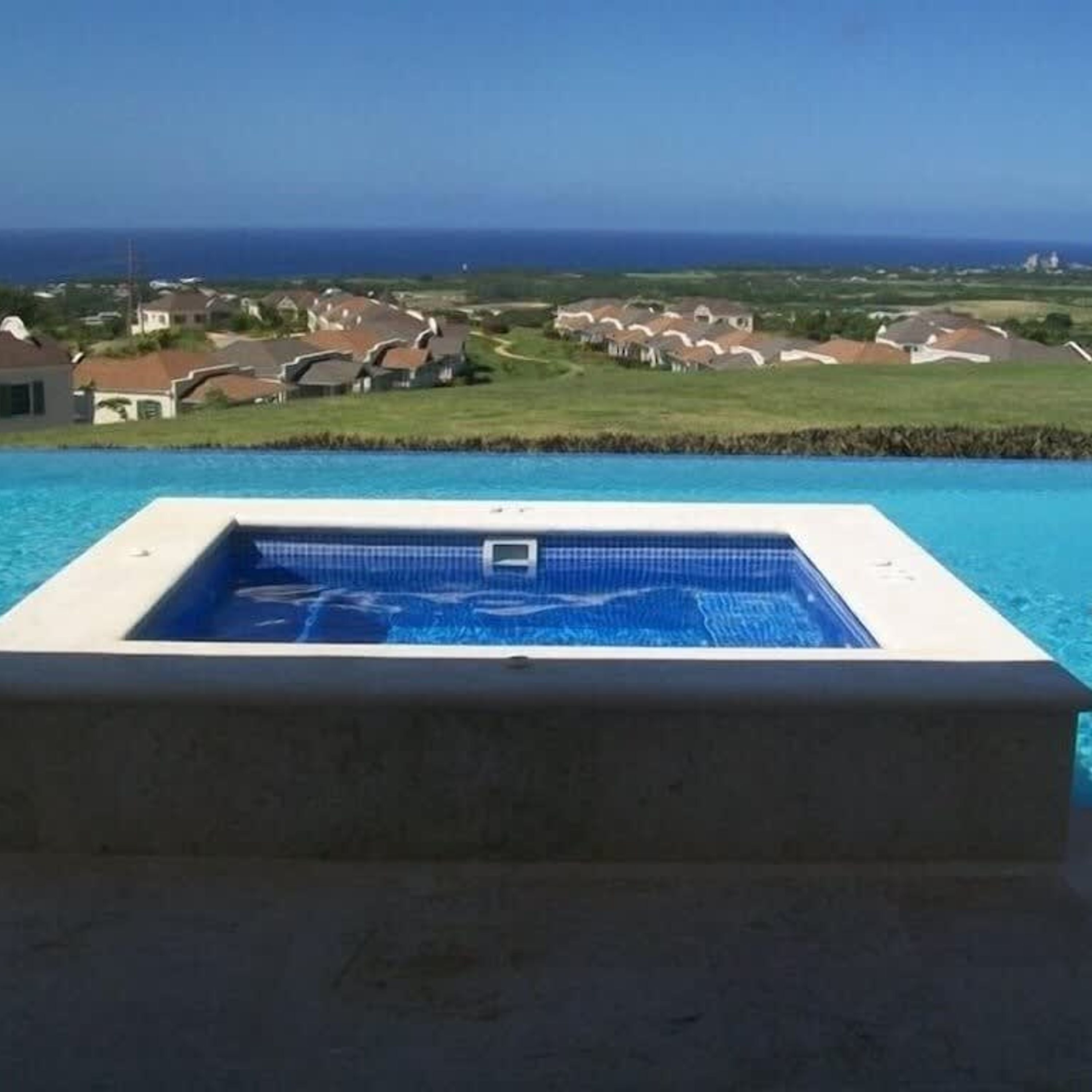 A swimming pool with a view of houses and the ocean.