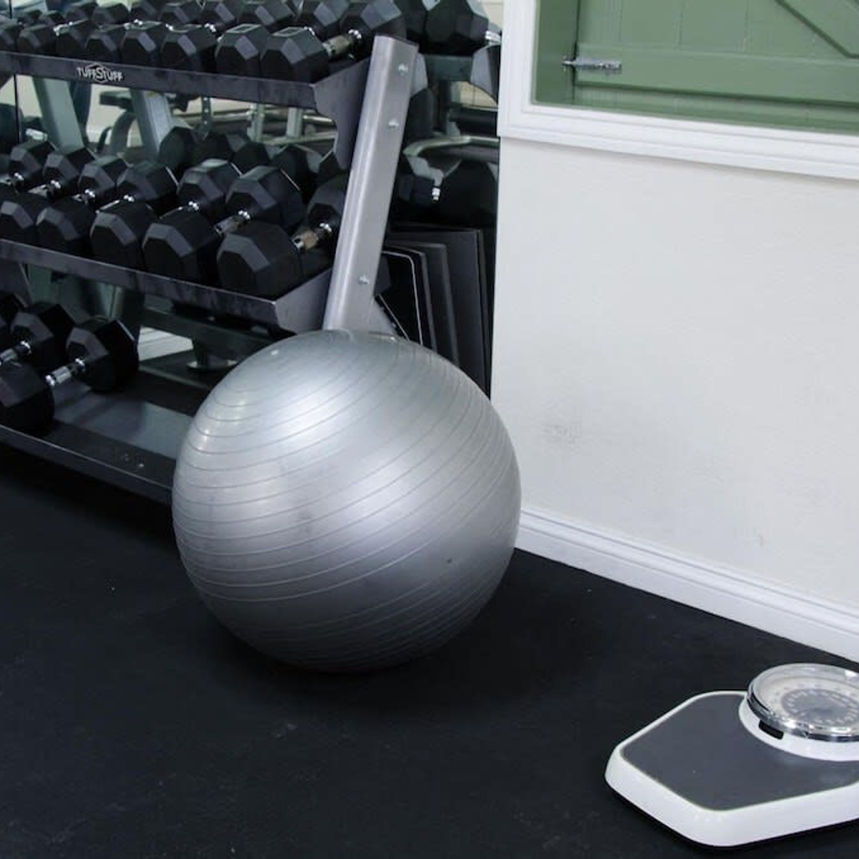 A gym with exercise equipment including dumbbells, a large exercise ball, and a weight scale.