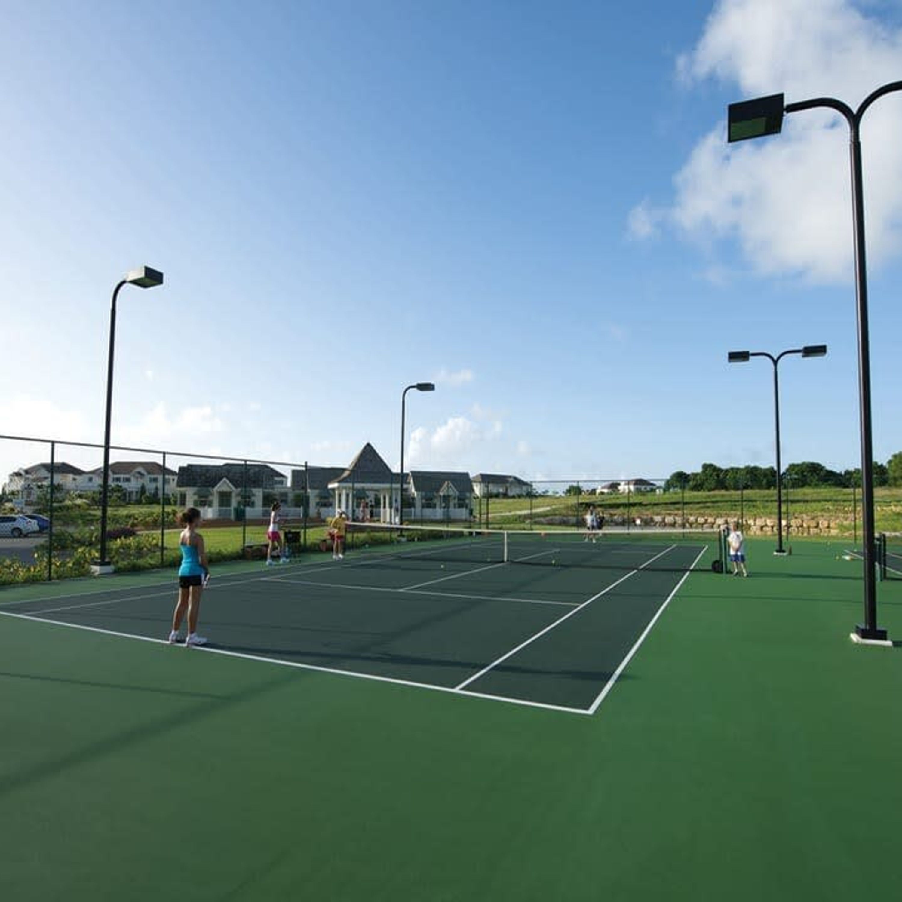 Ein Tennisplatz im Freien mit mehreren Spielern, umgeben von Häusern und blauem Himmel.