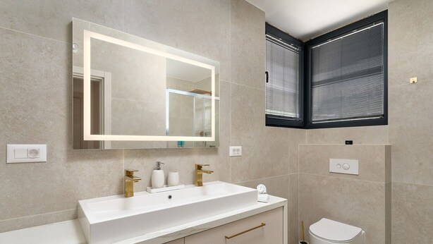 Un baño moderno con un espejo grande, dos lavamanos, un inodoro y una ventana con persianas.