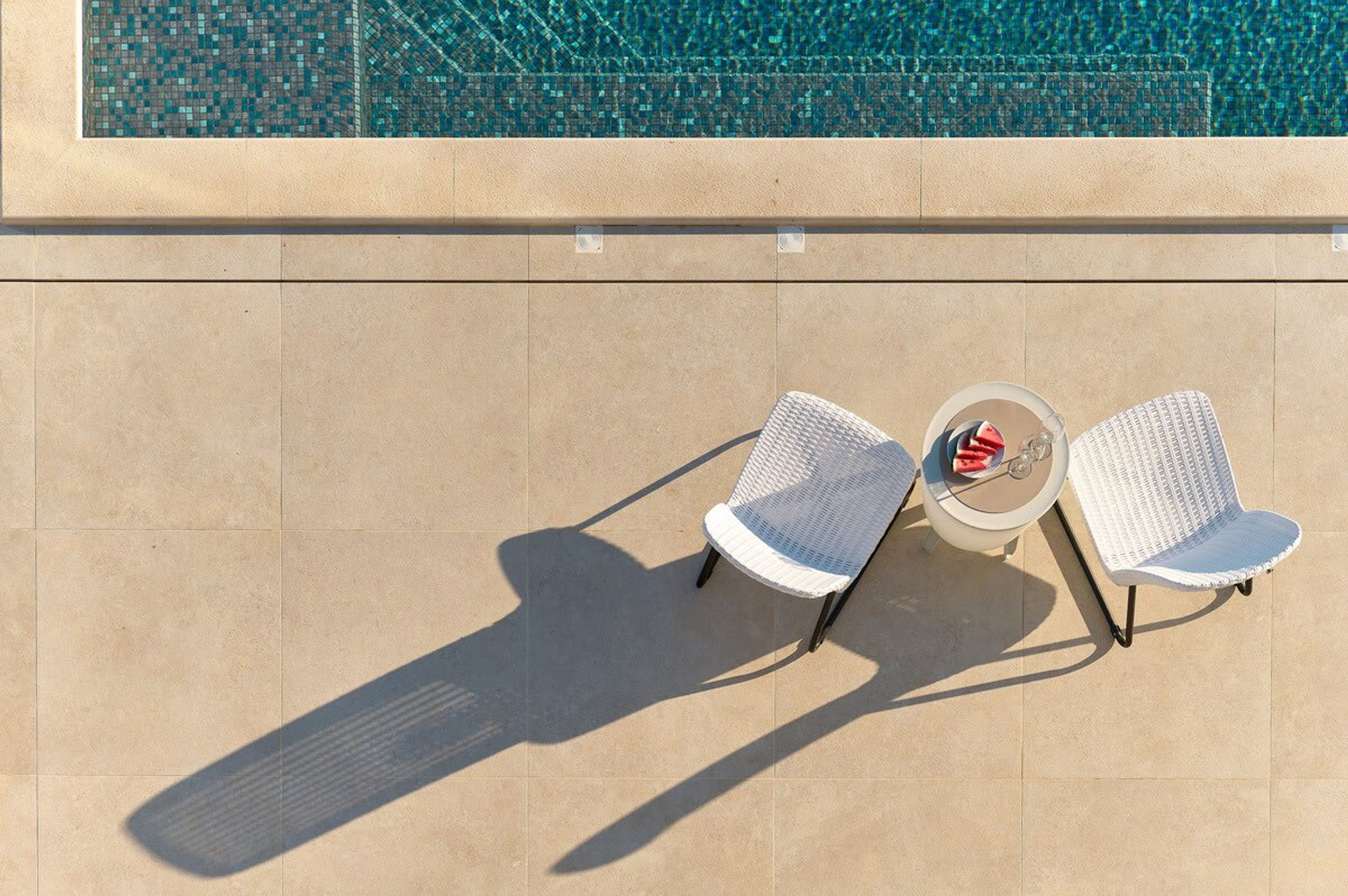 Deux chaises en osier blanches, avec une petite table ronde placée entre elles, sont disposées sur une terrasse carrelée.