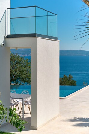 Ein moderner Außenbereich mit Pool, mit Blick auf das klare, blaue Meer und sanfte Hügel in der Ferne.
