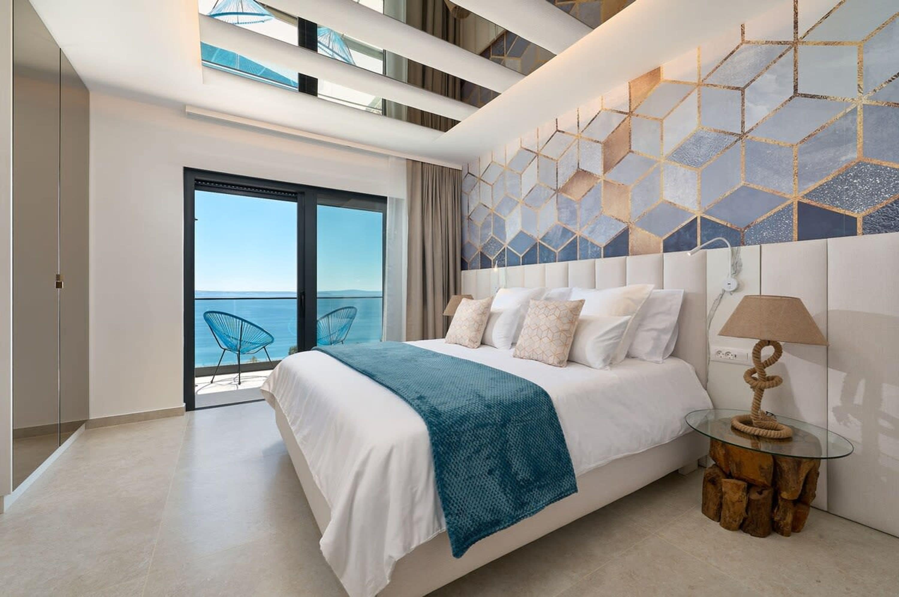A modern hotel room with a large bed, a glass coffee table, and a view of the sea.