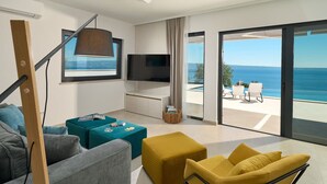 A modern living room with a large TV, a sofa, a coffee table, and a yellow armchair. There is a balcony with a view of the sea. - Villa Sunset - Luxury Adriatic Sea View Estate (Podstrana)