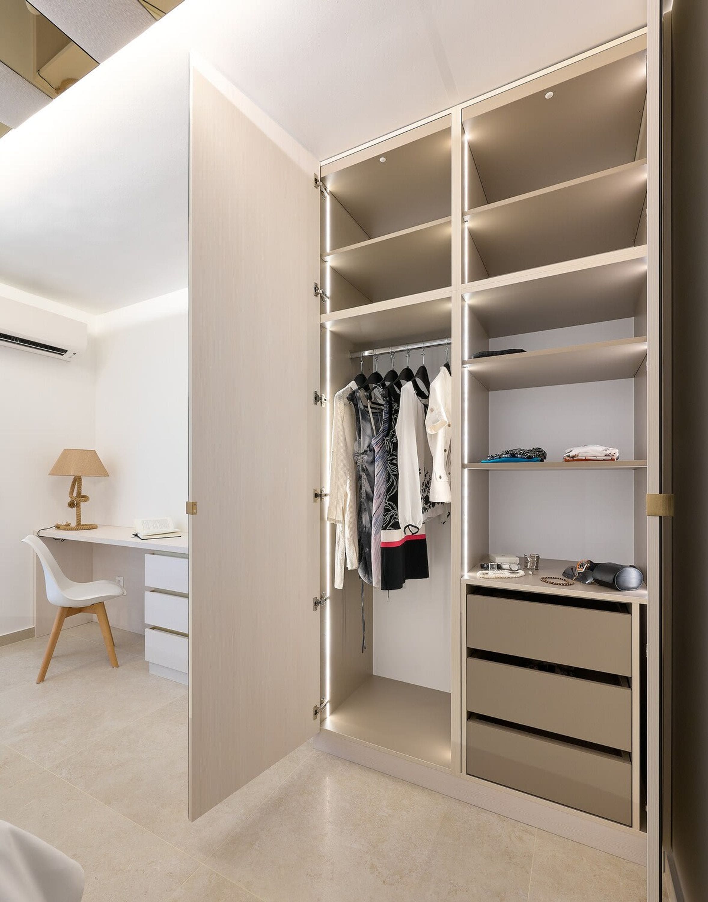 A walk-in closet with multiple shelves and hanging space, a desk with a lamp, and a chair.